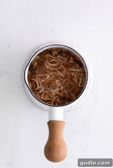 Thinly sliced shallots frying in avocado oil in a small saucepan.
