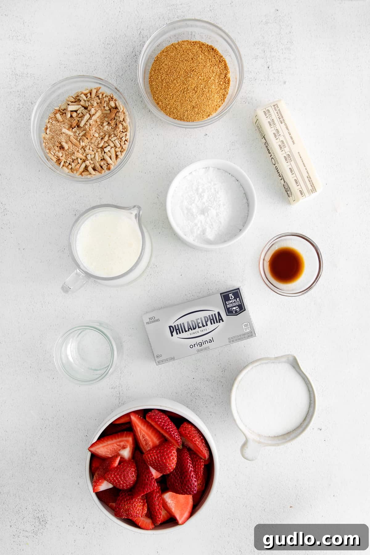 Fresh ingredients for strawberry cream cheese pie displayed neatly in bowls on a wooden surface.