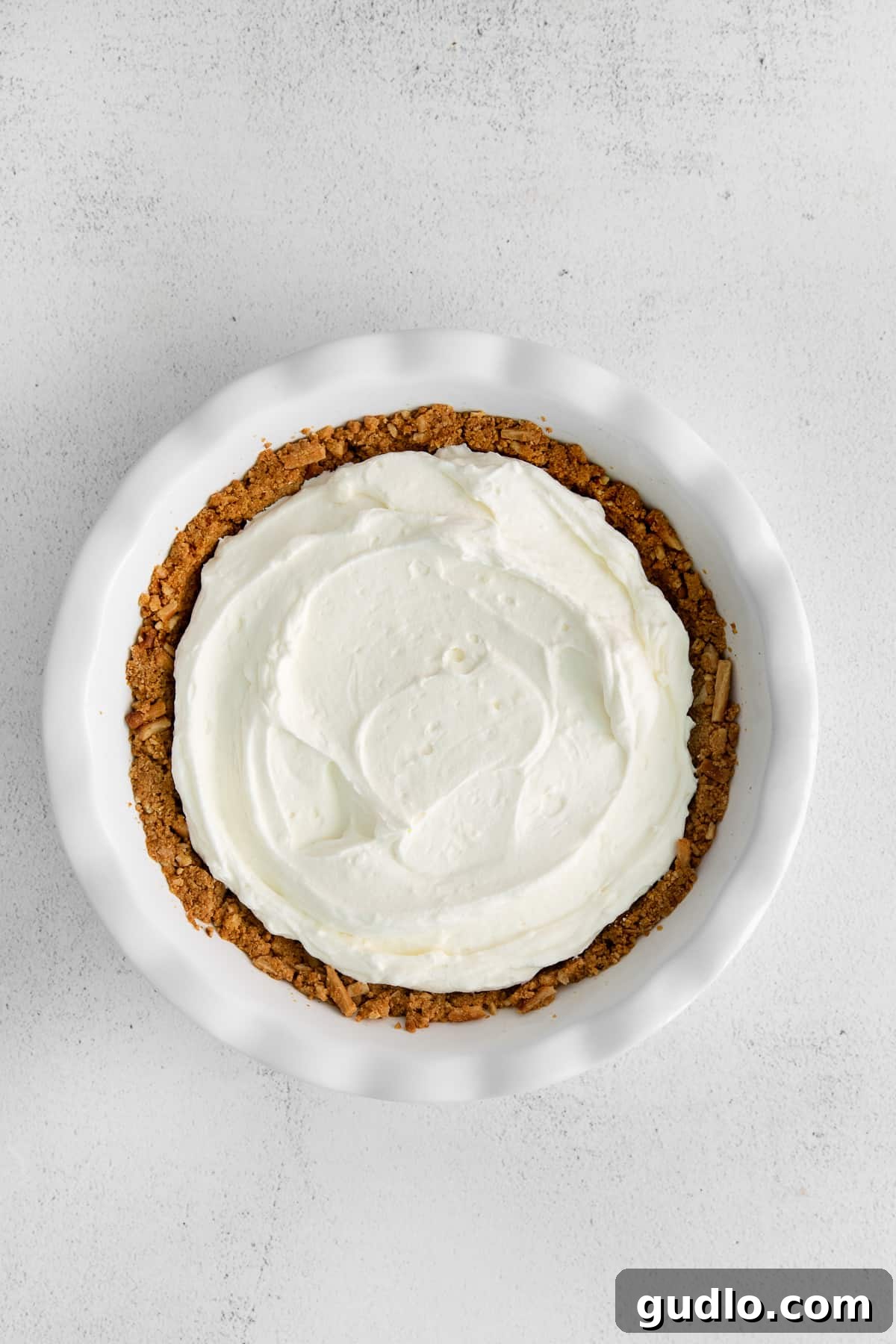 Cream cheese pie filling meticulously smoothed into a baked graham cracker crust, ready for the strawberry topping.