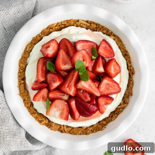 A white plate holds a mouthwatering slice of strawberry cream cheese pie filled with strawberries and cream cheese, garnished with mint.