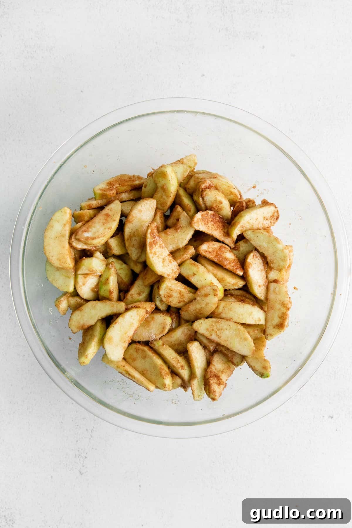Bowl of thinly sliced Granny Smith apples coated in a glistening sugar and spice mixture, ready for the pie.