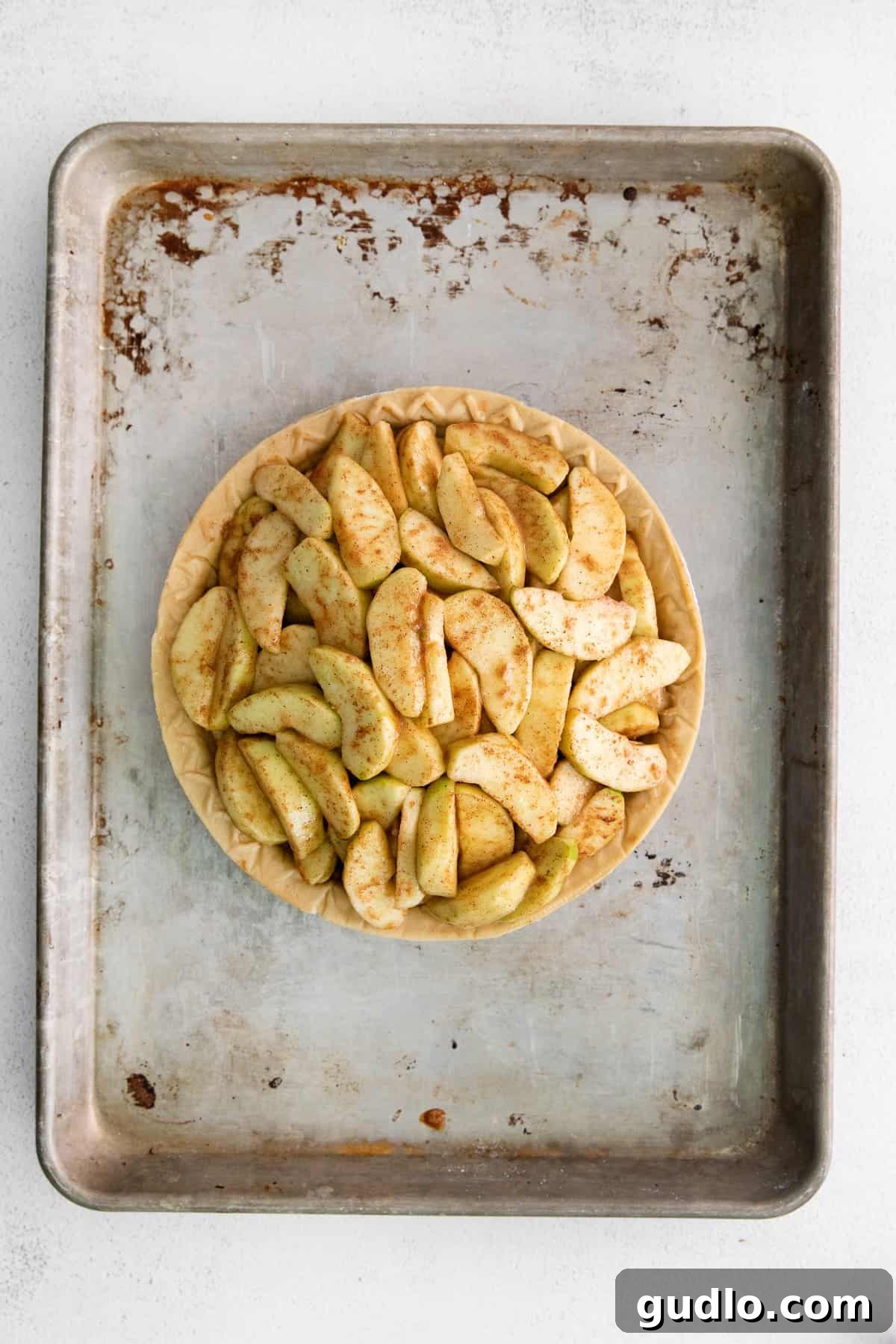 Unbaked apple pie in a crust on a baking sheet, showing the apple filling mounded high.