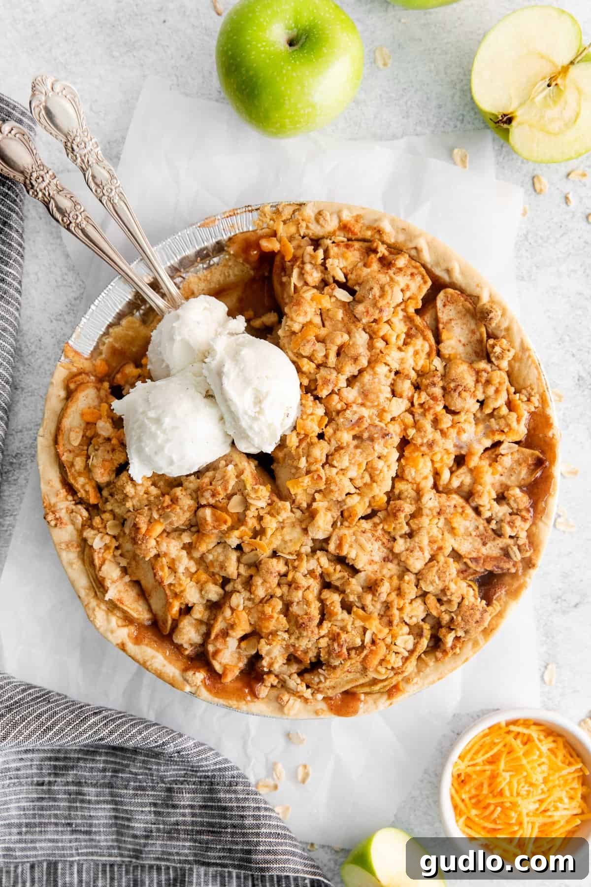 A delectable slice of apple pie with cheese, beautifully topped with a scoop of melting vanilla ice cream, on a white plate.