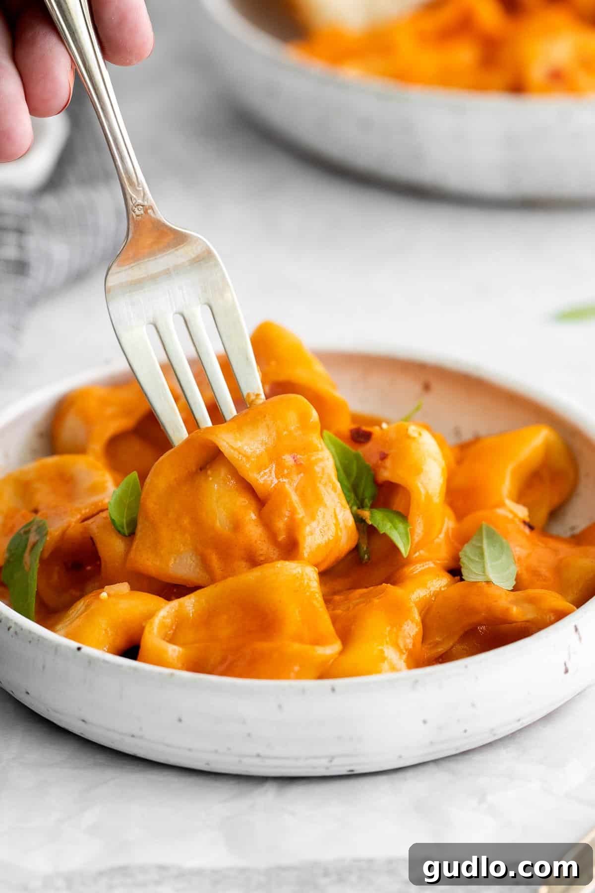 Vodka Blush Tortellini 2 A fork piercing a plump cheese tortellini, glistening with rich, creamy vodka sauce, inviting a delectable bite.