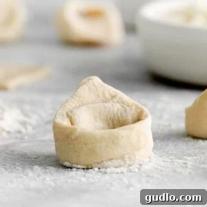 Vodka Blush Tortellini 4 A close-up of delicate homemade tortellini dough on a wooden cutting board, meticulously rolled and ready for filling.