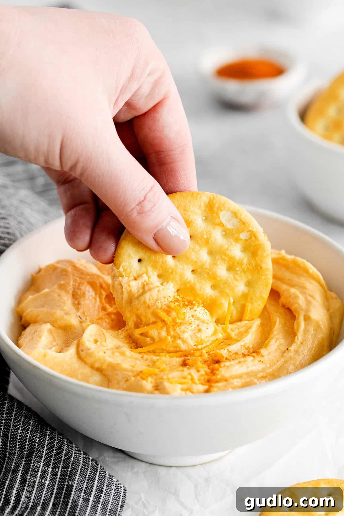 Easy Homemade Cheese Spread: 6 Ingredients, 15 Minutes to Creamy Perfection Person dipping a crispy cracker into a bowl of creamy homemade cheese spread, highlighting its smooth texture and golden hue.
