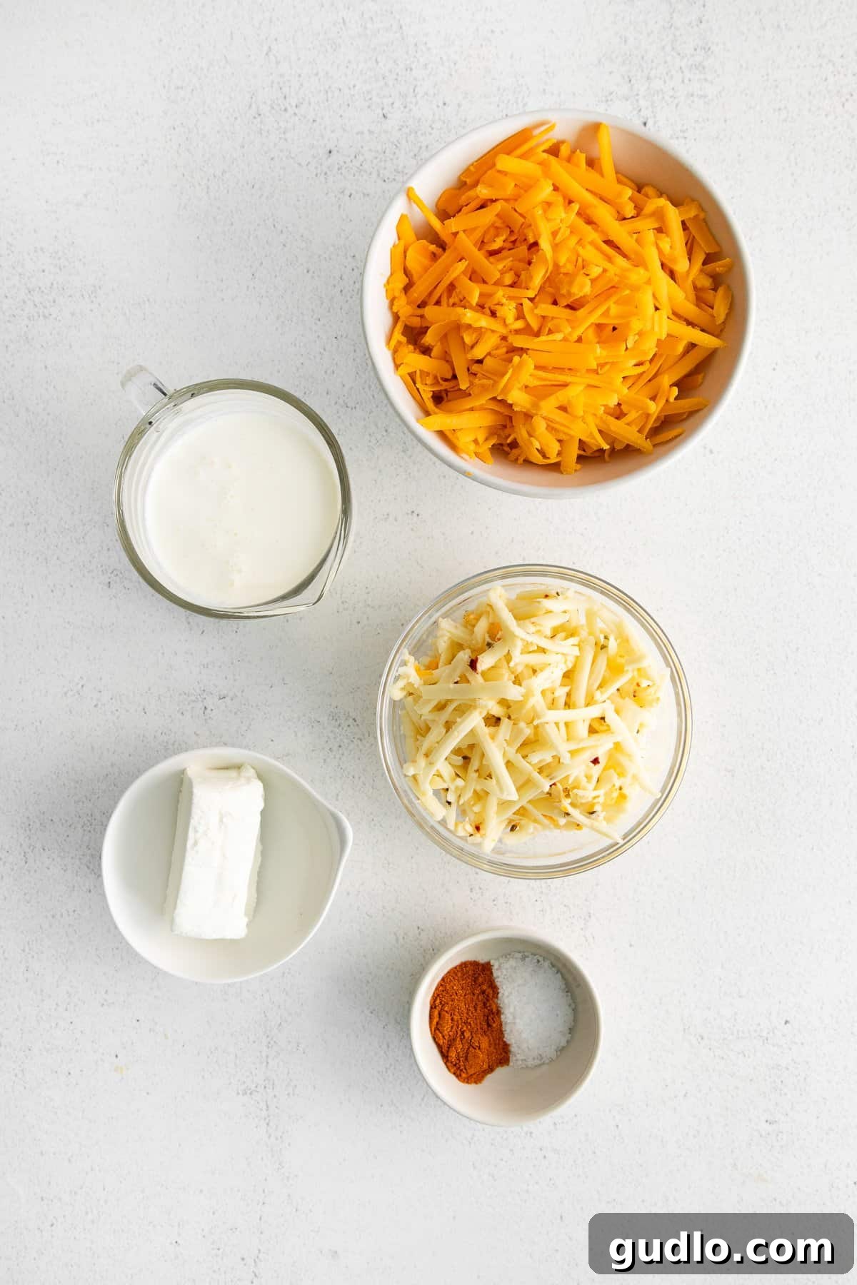 Simple Ingredients for Your Best Homemade Cheese Spread Bowls filled with the six essential ingredients for homemade cheese spread: shredded cheddar, pepper jack, cream cheese, half and half, kosher salt, and paprika.