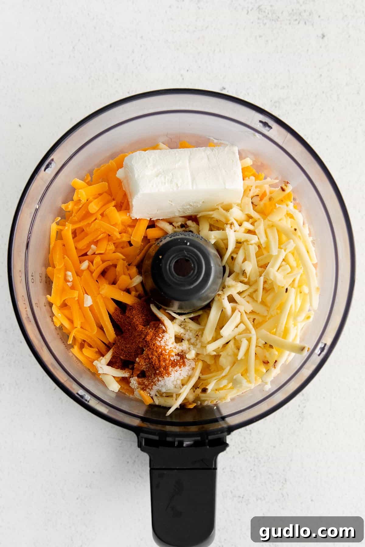 Blending Ingredients for the Ultimate Homemade Cheese Spread Shredded cheddar, pepper jack, cream cheese, half and half, salt, and paprika being added to a food processor bowl, ready for blending into a delicious homemade cheese spread.