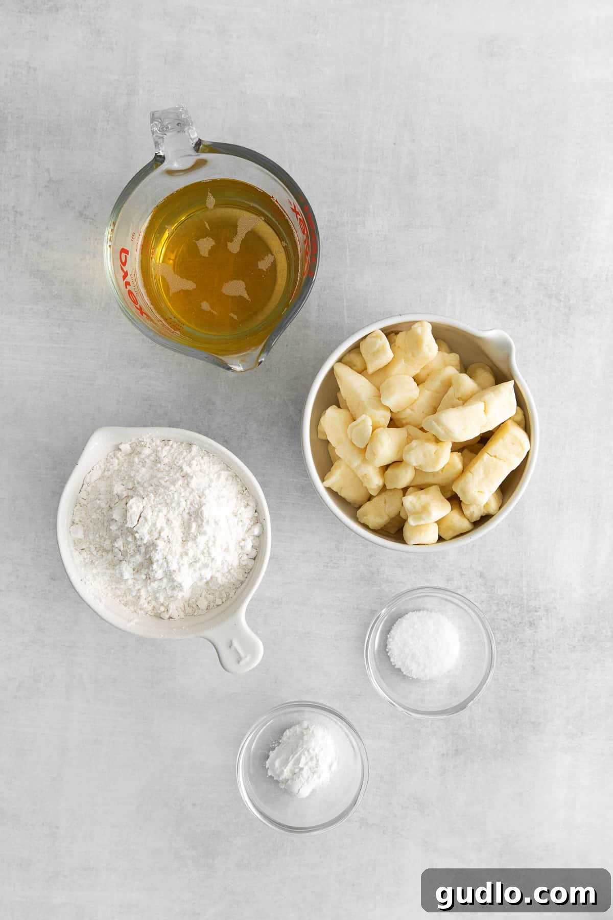 Ingredients for Homemade Fried Cheese Curds Essential ingredients for homemade fried cheese curds neatly arranged on a kitchen countertop, including a bag of fresh cheese curds, all-purpose flour, a bottle of light beer, and cooking oil.