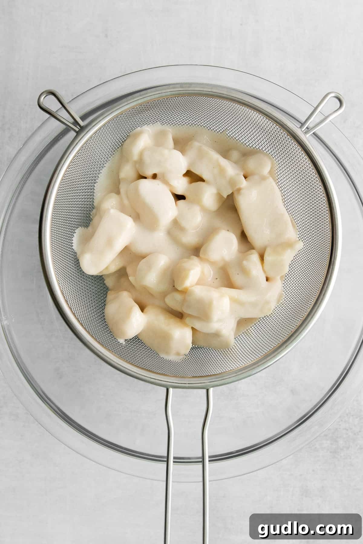 Draining Excess Batter from Cheese Curds A close-up view of batter-covered cheese curds resting in a metal strainer, prepared and ready for deep frying.