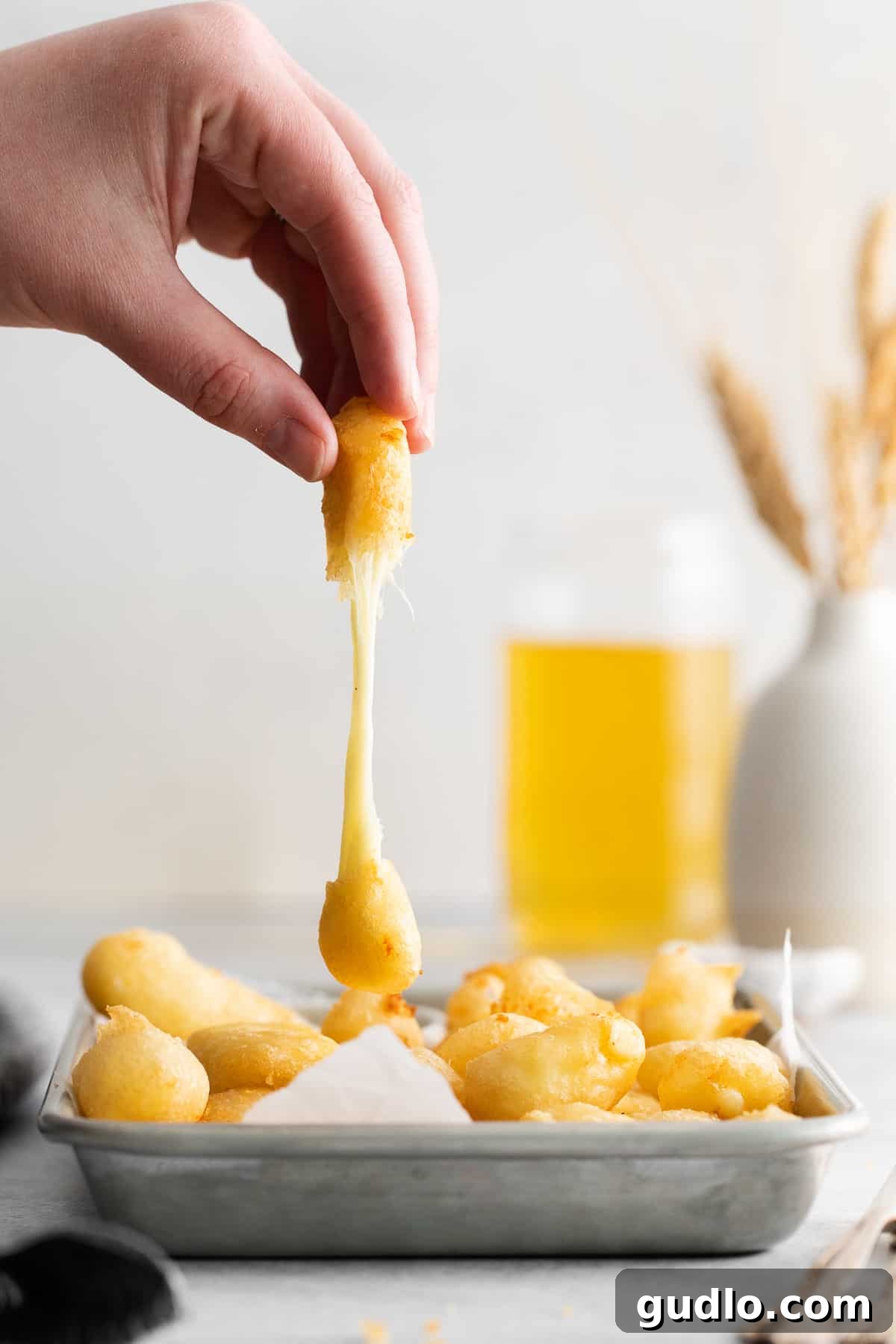 Single Fried Cheese Curd A hand gently holding a single, perfectly golden-brown and crispy fried cheese curd, showcasing its inviting texture.