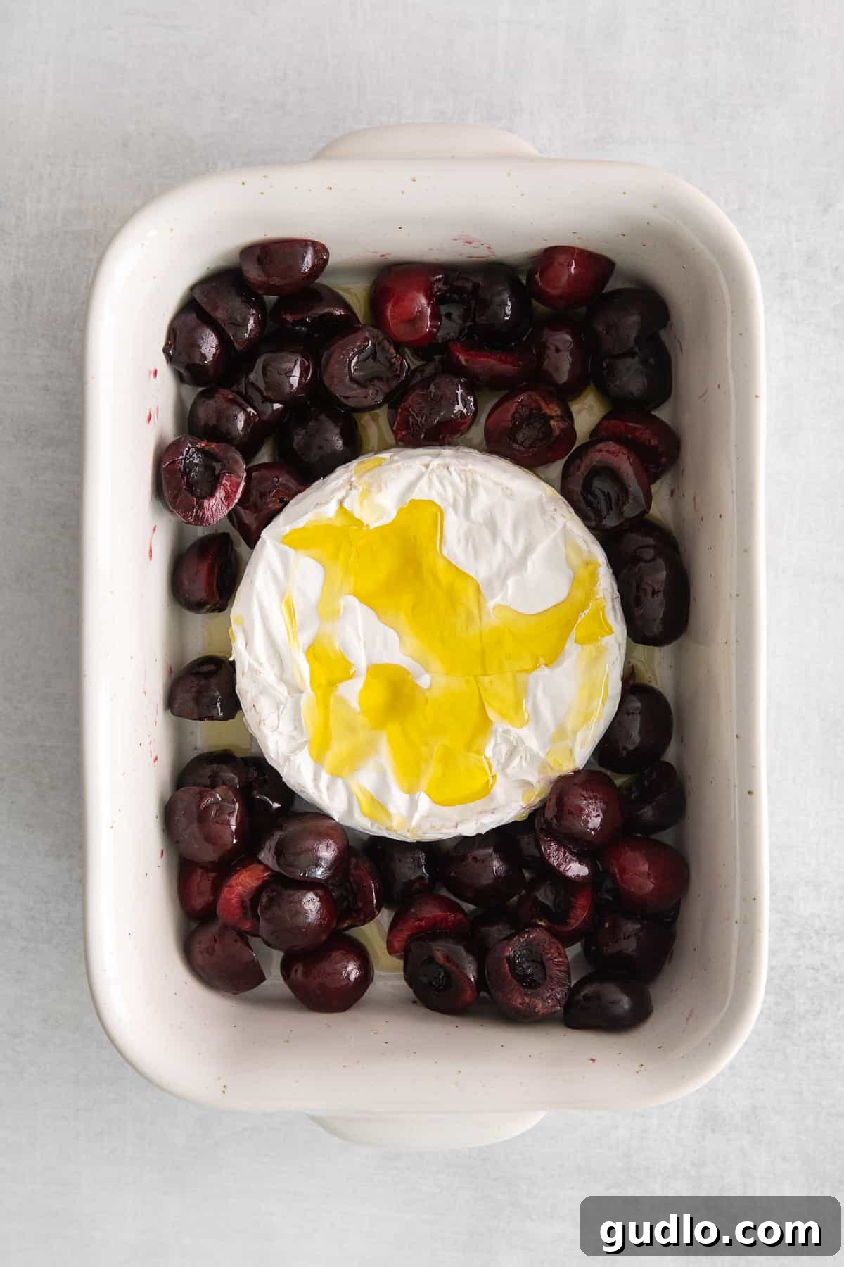 A wheel of young brie cheese lightly drizzled with olive oil, ready for grilling.