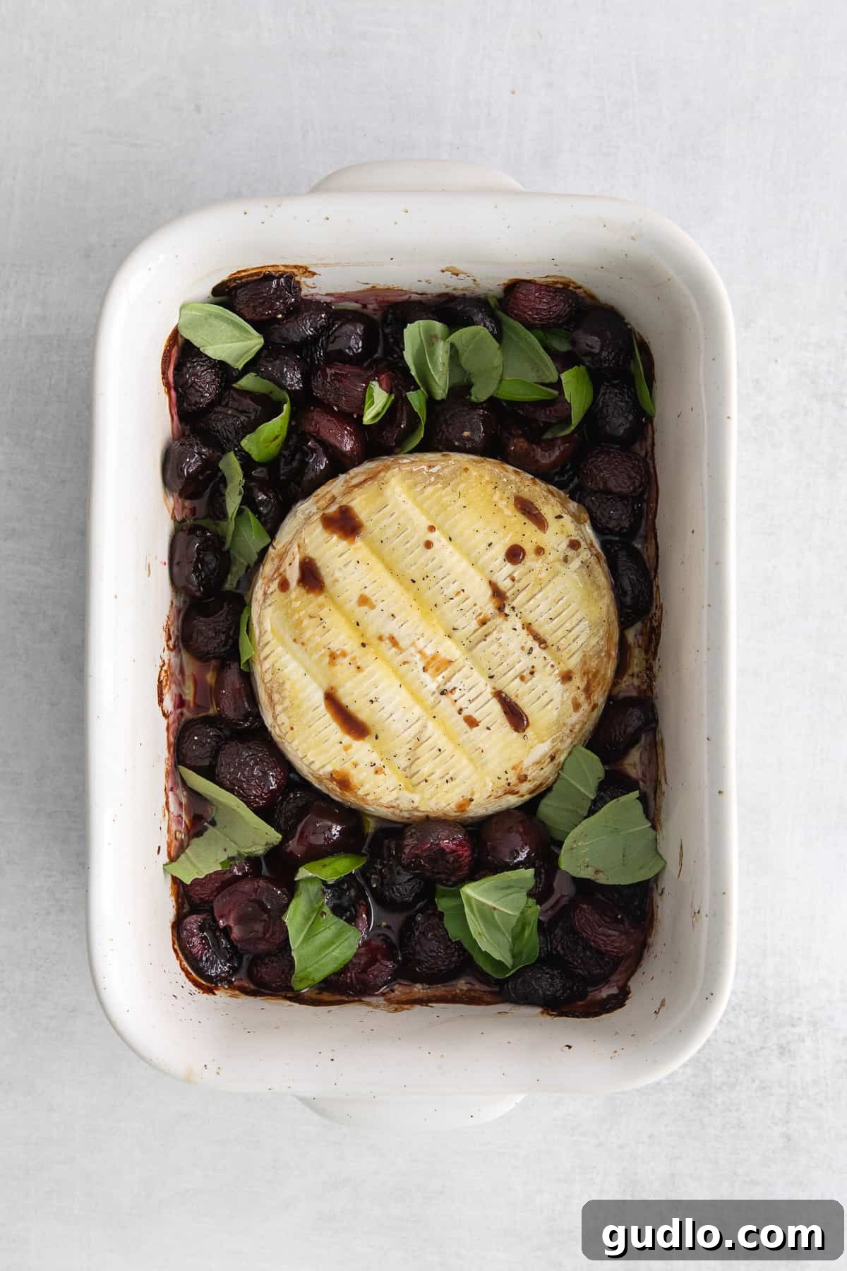 Glorious grilled brie cheese topped with a vibrant balsamic drizzle and fresh basil leaves.