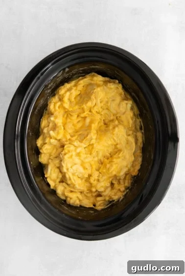 A crock pot filled with creamy mac and cheese after cooking, with the final cheese being melted in.