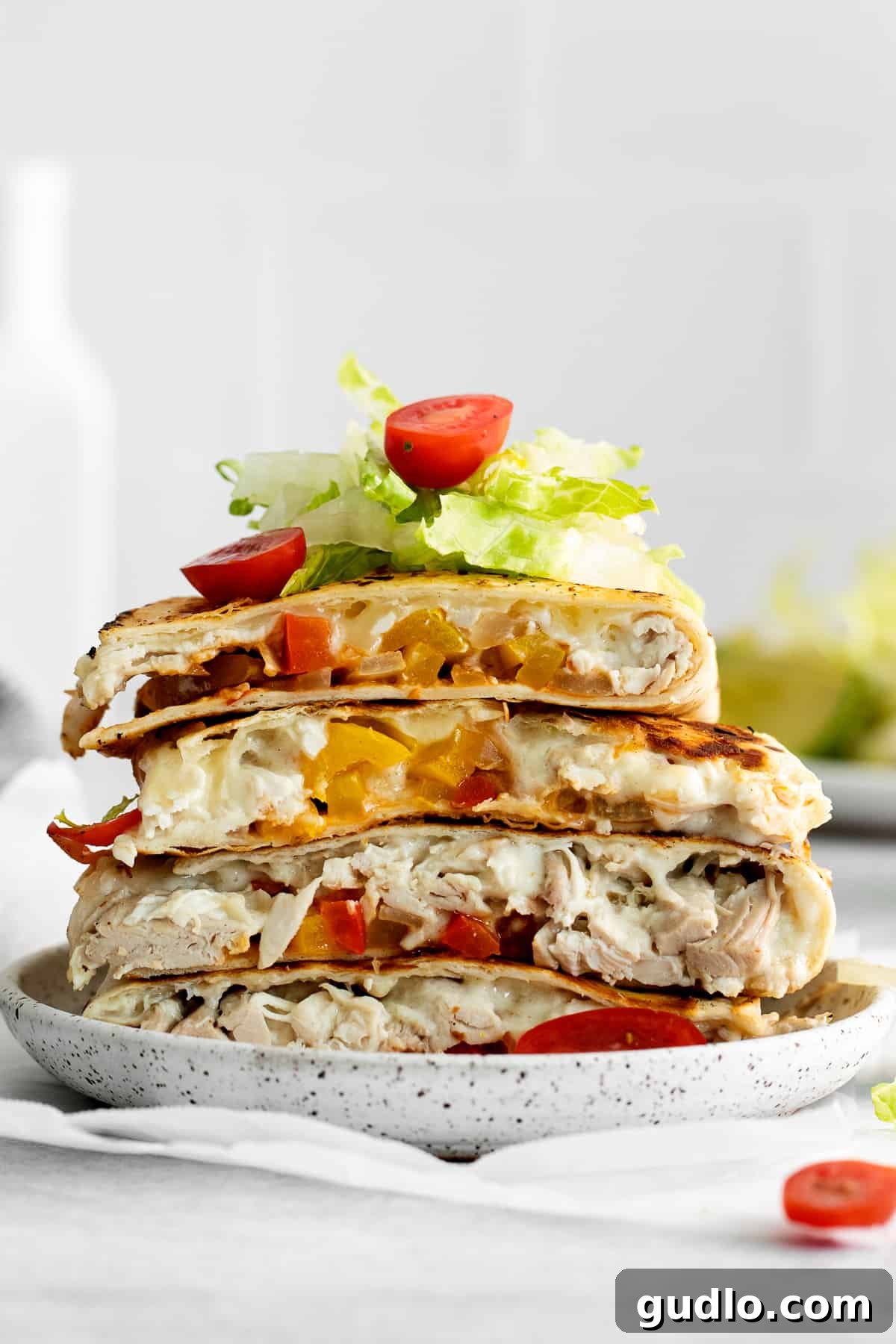 Stacked chicken quesadillas topped with fresh tomatoes and crisp lettuce, showcasing a delicious meal.
