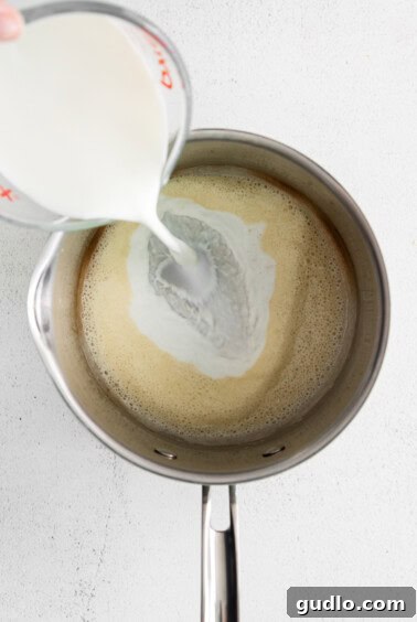 A person carefully pouring milk into a saucepan to create a smooth sauce.