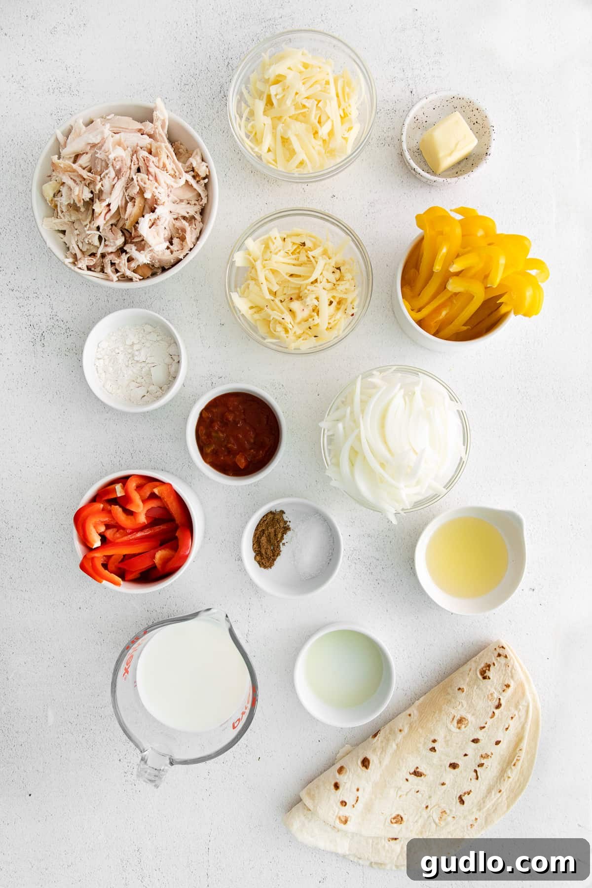 Arrangement of fresh ingredients for chicken quesadillas in various bowls, including bell peppers, shredded chicken, and cheese.