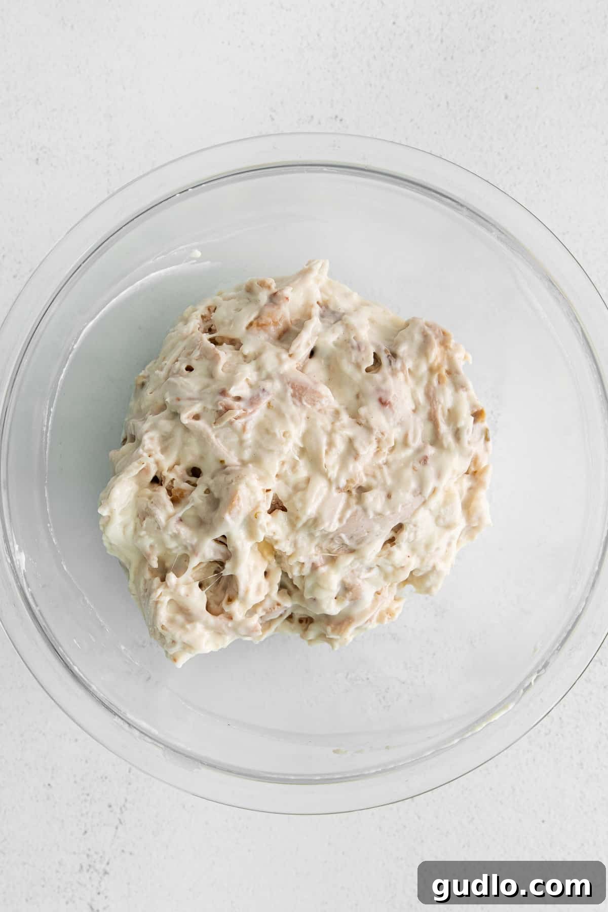 Bowl of smothered shredded chicken, thoroughly coated in a rich, creamy cheese sauce.