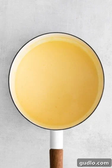 a yellow sauce in a pan with a wooden spoon.