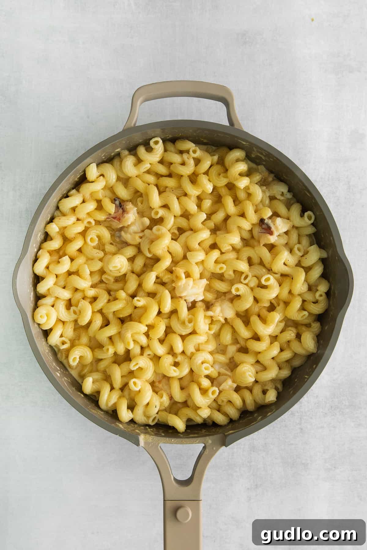 Decadent Lobster Macaroni 4 Creamy mac and cheese sauce being stirred with cavatappi noodles in a large pot.