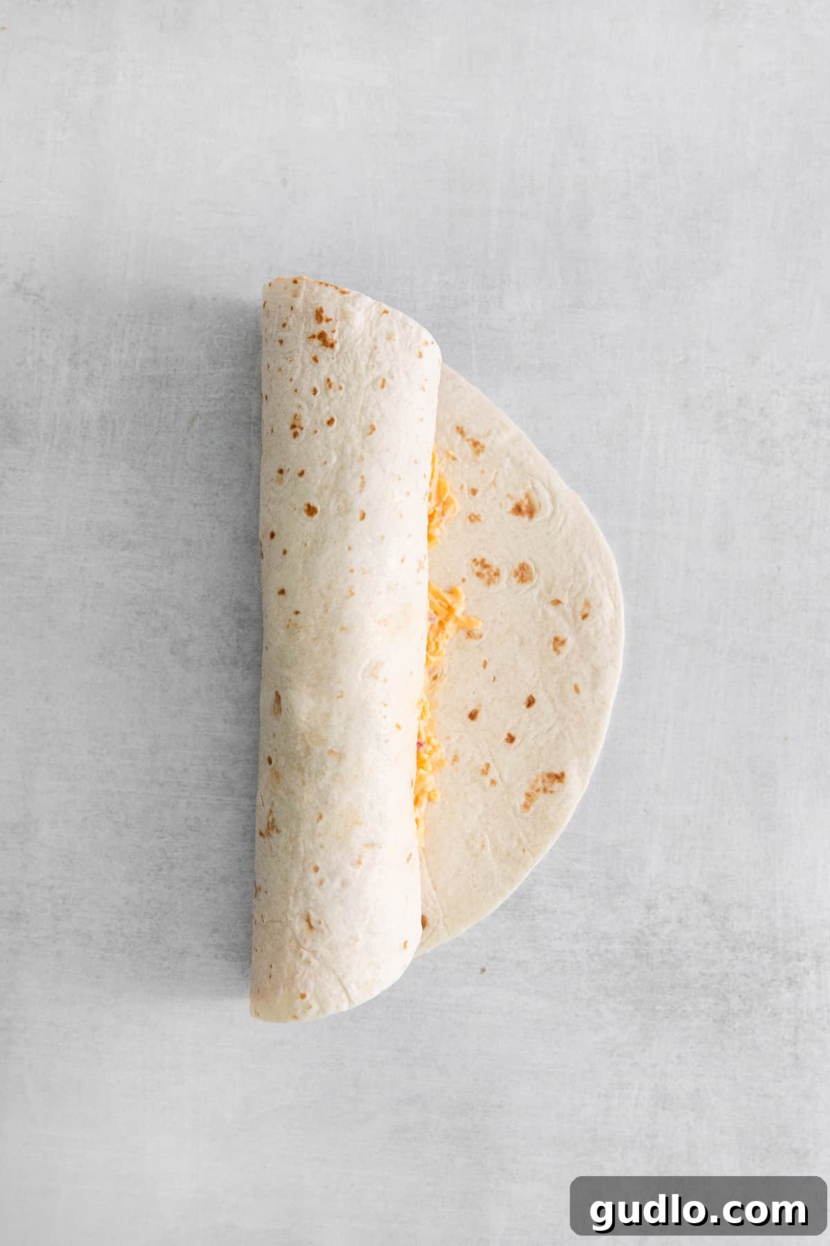 A tightly rolled tortilla, filled with pimento cheese, turkey, and vegetables, ready to be sliced into individual pinwheels.