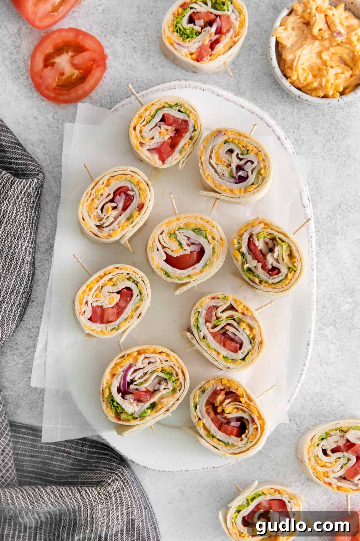 Beautifully arranged sliced pimento cheese pinwheels on a white plate, showcasing the vibrant layers of ingredients: pimento cheese, turkey, lettuce, tomato, and red onion.