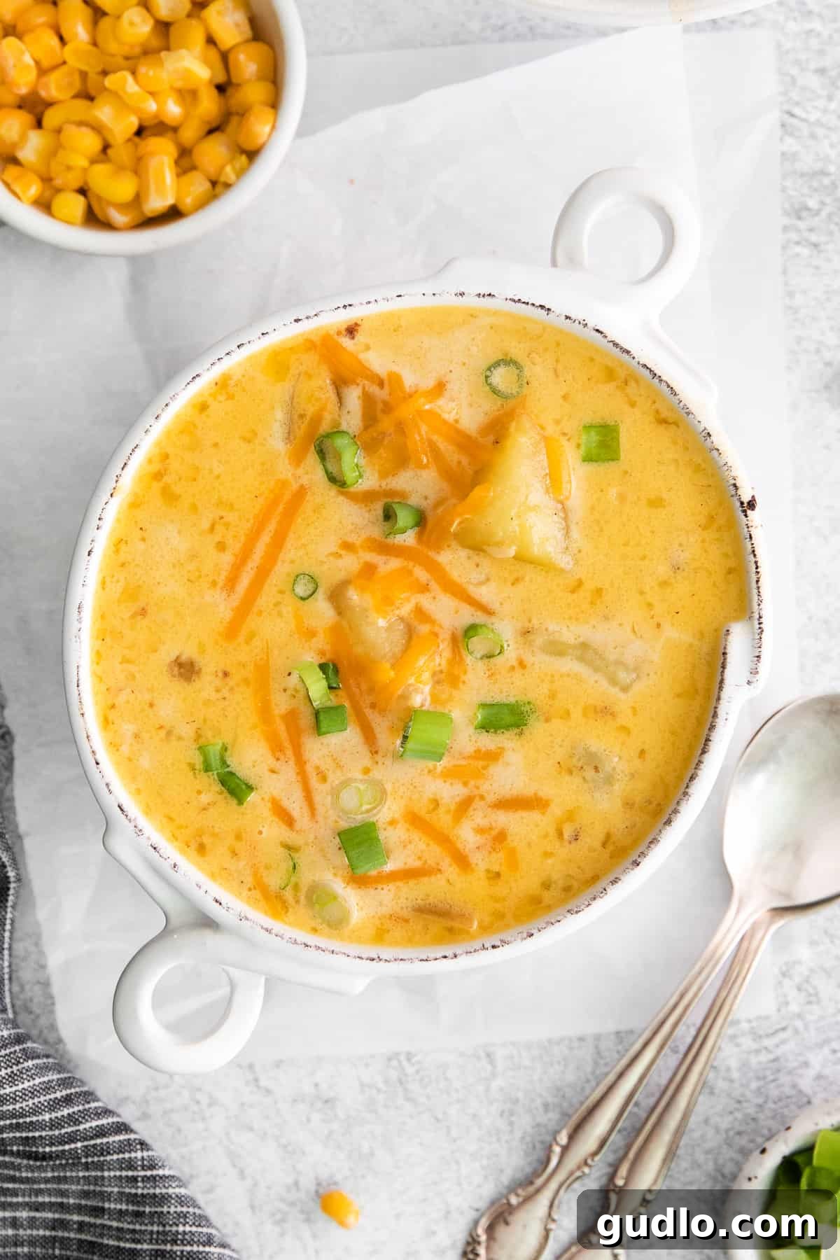 The Best Cheesy Corn Chowder Recipe A steaming bowl of cheesy corn chowder, garnished with fresh cheddar and green onions.