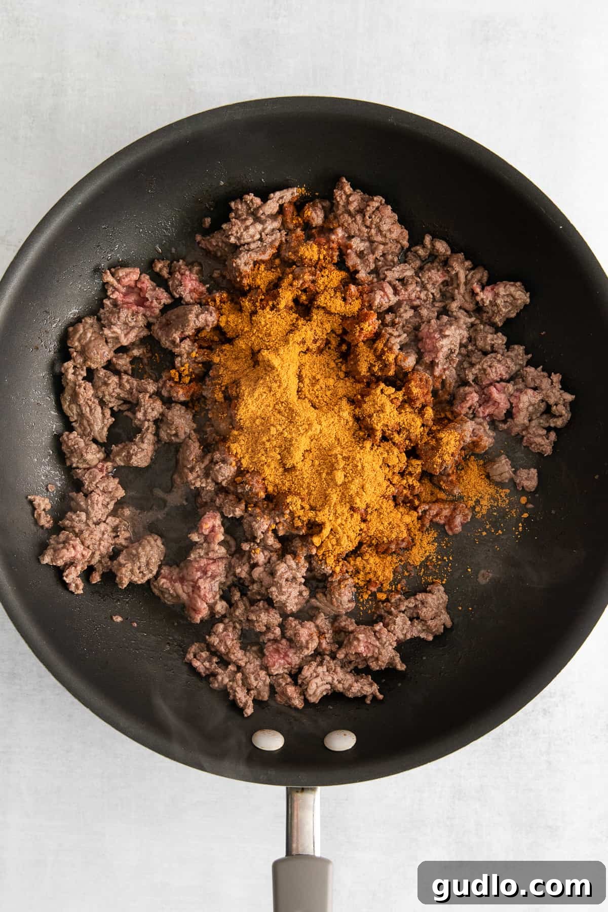 Cooking seasoned ground beef in a skillet, preparing the delicious chili base.