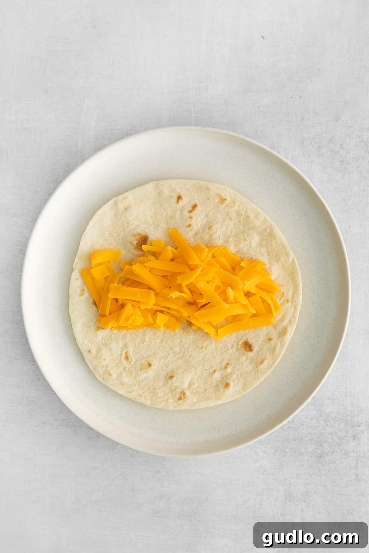Shredded cheddar cheese sprinkled onto a warm tortilla, ready for the filling.