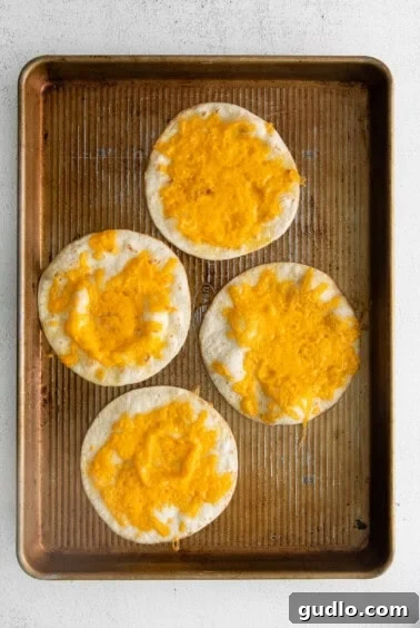 Four cheesy tortillas baking on a sheet pan, becoming golden and crispy.