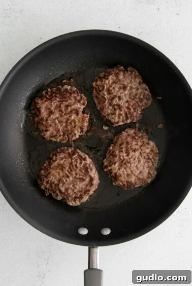 Four sizzling hamburger patties cooking in a frying pan.