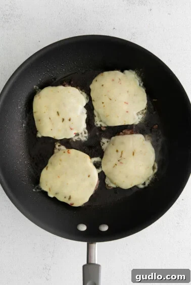 Melting pepperjack cheese on top of burger patties in a skillet.