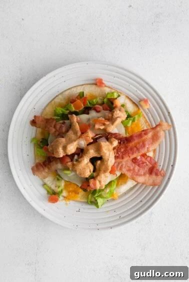 A plate showing the construction of a quesadilla burger with layers of bacon, lettuce, and tomatoes.