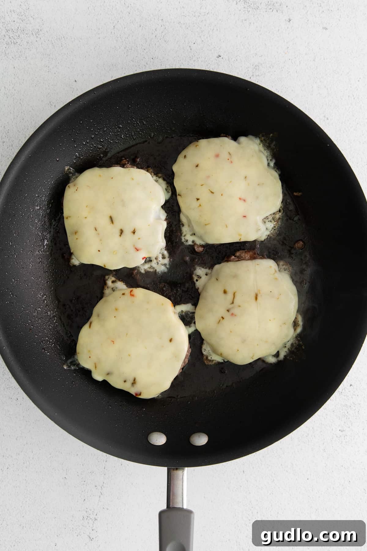 Melting pepper jack cheese draped over juicy burger patties in a hot skillet, ready for assembly.