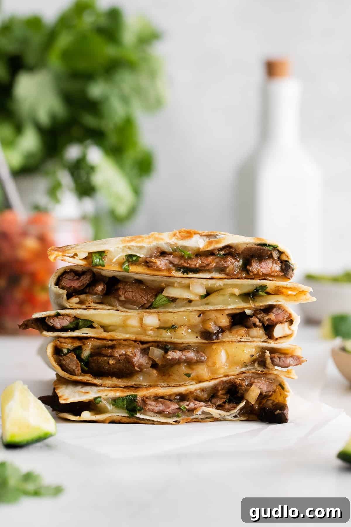 The ultimate steak quesadilla is made with flank steak, mushrooms, onion, and tons of Monterrey Jack cheese! Stack of ultimate steak quesadilla slices on a cutting board, garnished with cilantro.
