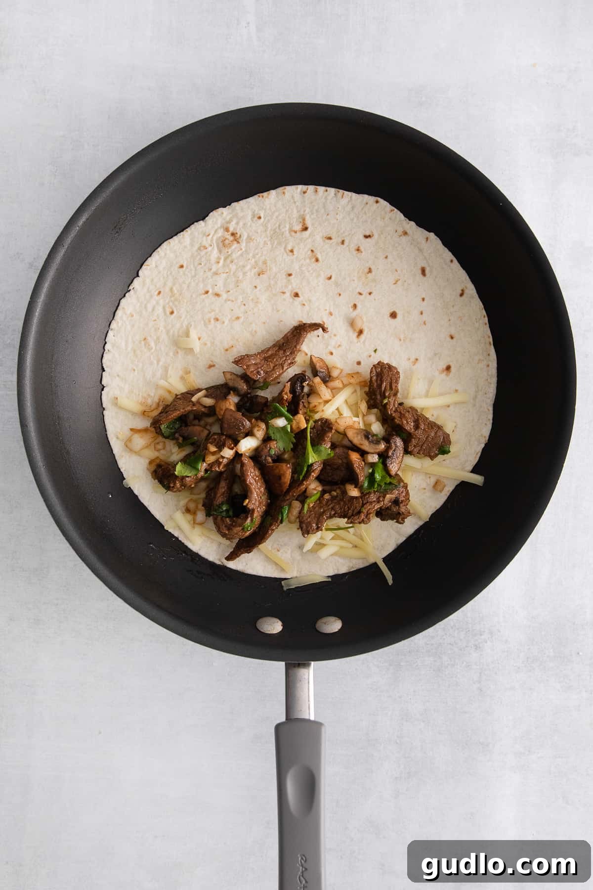The ultimate steak quesadilla is made with flank steak, mushrooms, onion, and tons of Monterrey Jack cheese! Cheese, steak, and onions layered on one half of a tortilla in a hot skillet, ready to be folded.