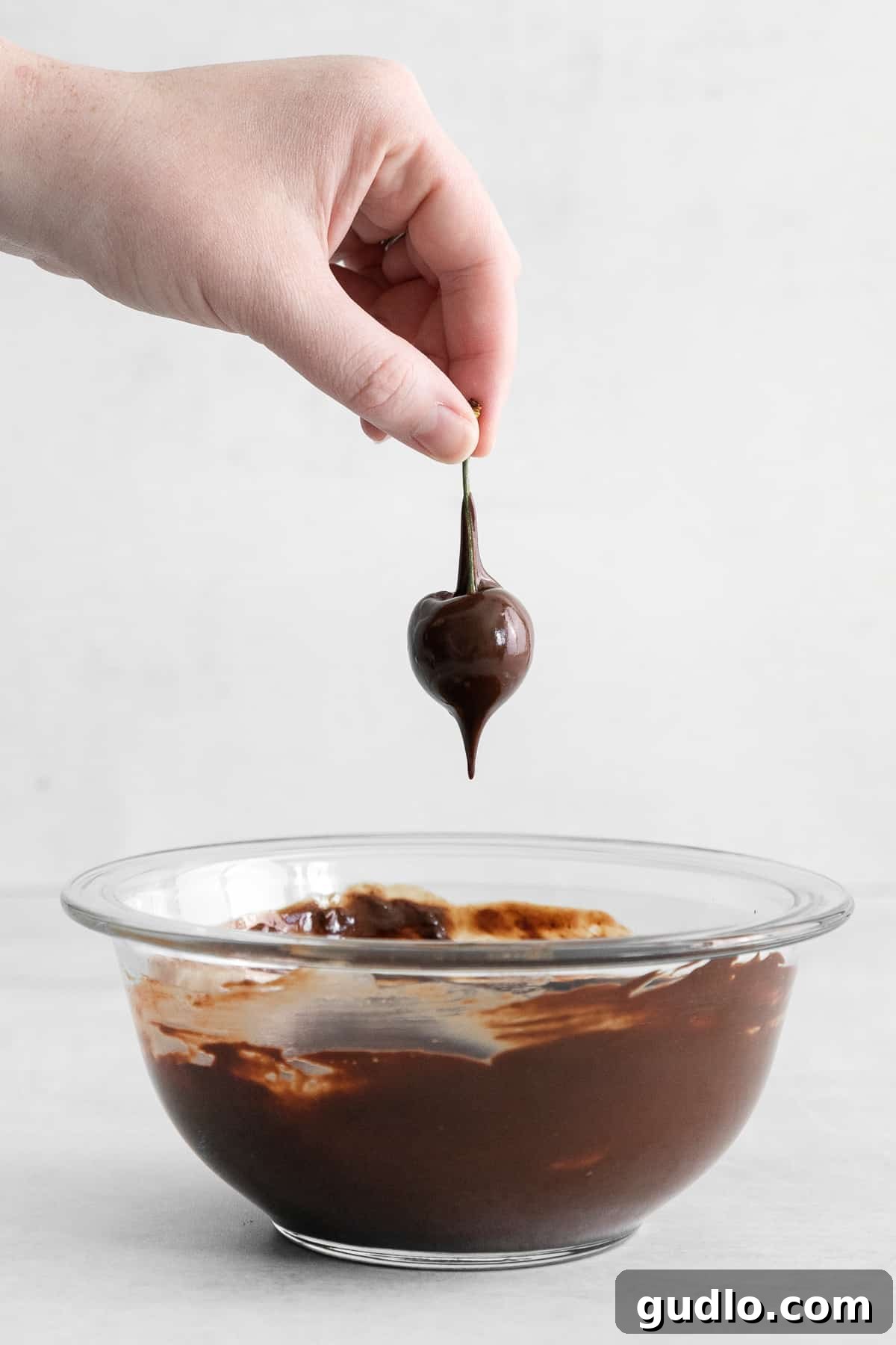 Velvet Cherry Mascarpone Chocolates 6 A fresh cherry being carefully dipped into a bowl of perfectly melted, glossy dark chocolate.