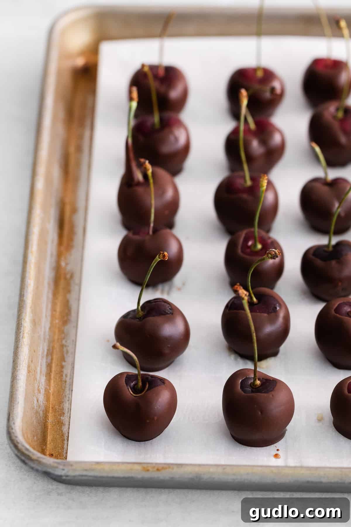 Velvet Cherry Mascarpone Chocolates 8 Freshly made chocolate covered cherries resting on parchment paper, allowing the chocolate to fully set.