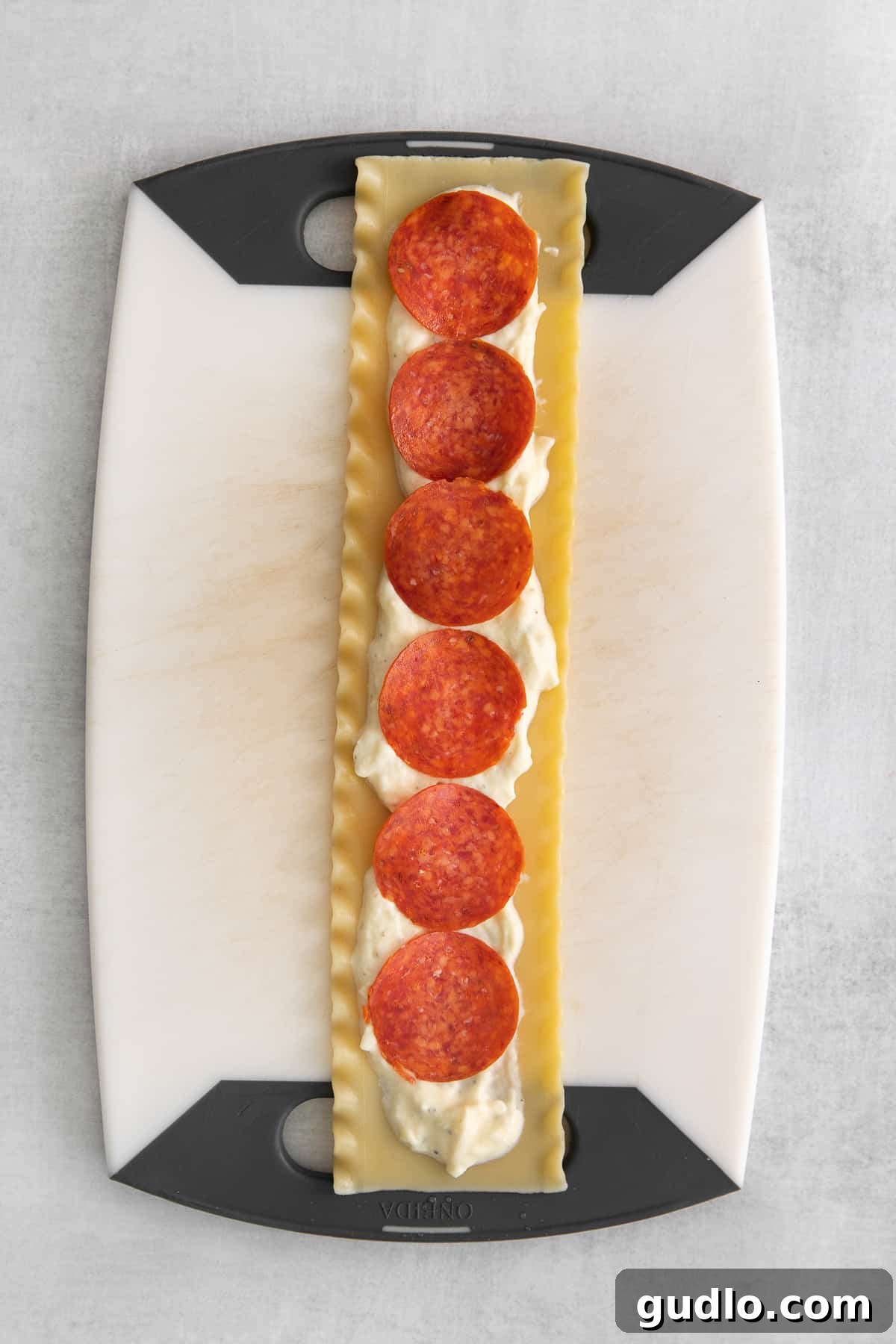 Assembling Delicious Pizza Lasagna Roll Ups Hands carefully rolling a lasagna noodle filled with cheese and pepperoni, preparing it for baking.