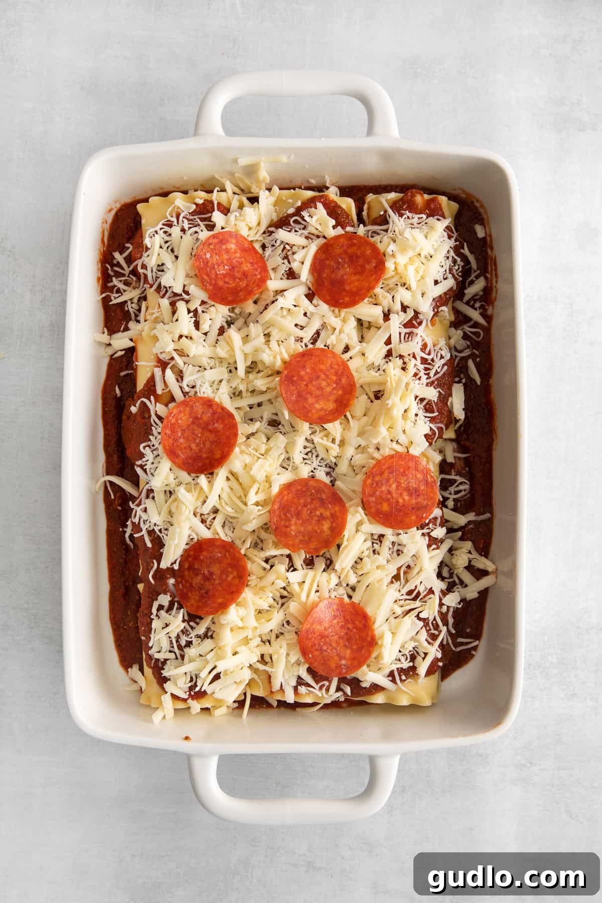 Pre-baked Pizza Lasagna Roll Ups with Pepperoni and Cheese Close-up of the assembled pizza lasagna roll ups, generously topped with pepperoni and a mix of shredded mozzarella and cheddar gruyere cheese, ready for baking.