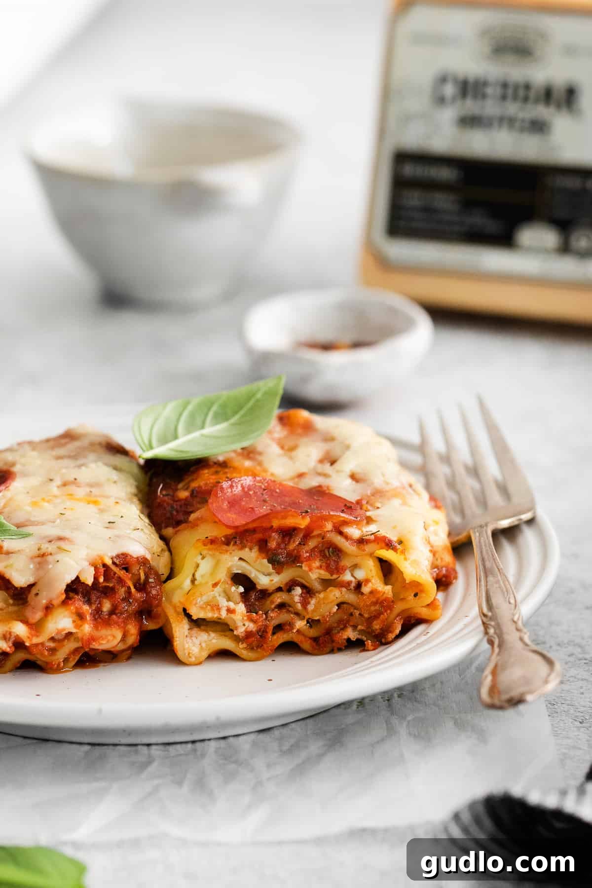Single Serving of Pizza Lasagna Roll Up A single pizza lasagna roll up on a white plate, ready to be enjoyed with a fork inserted into its rich layers.