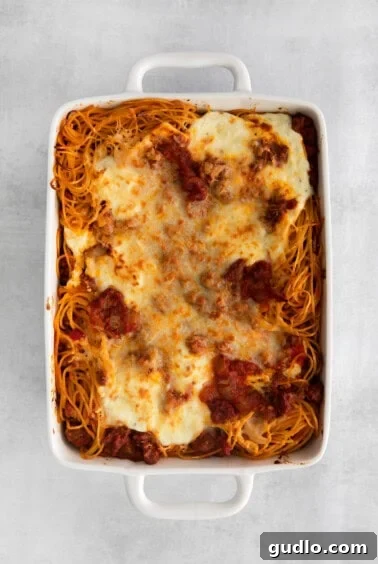 baked spaghetti in dish, covered with foil, and then uncovered to reveal golden cheese.
