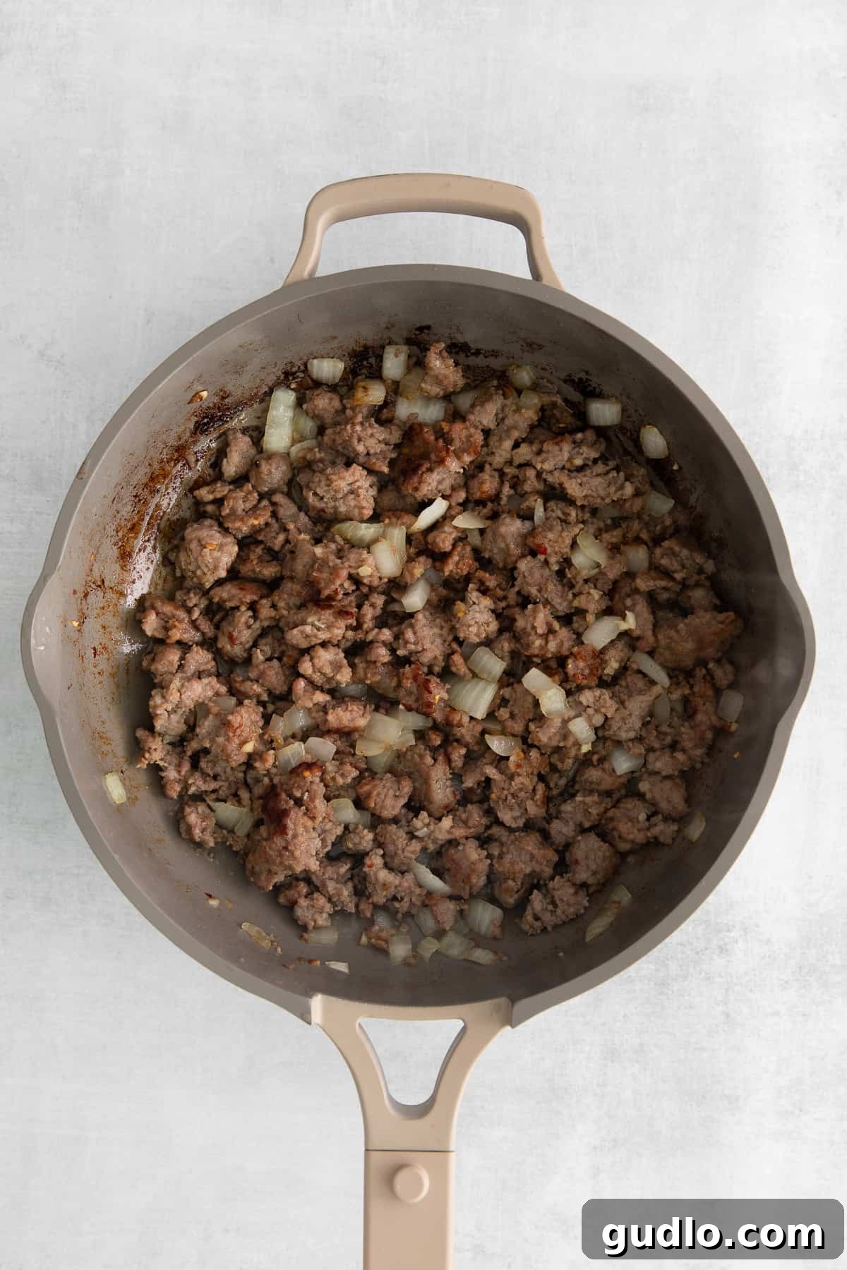Baked spaghetti with cream cheese is an excellent kid-friendly, weeknight meal that makes for great leftovers! close-up of ground pork and onions sizzling in a pan for the baked spaghetti sauce.