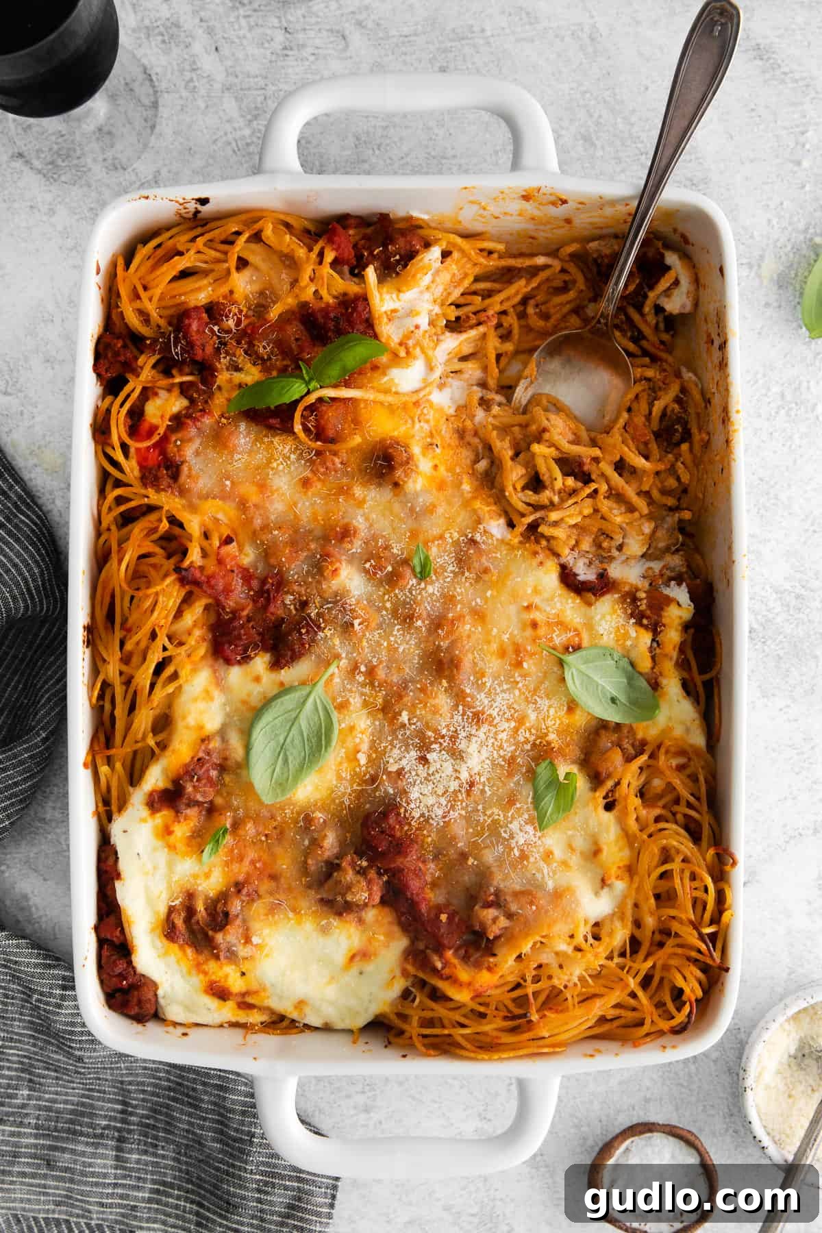 Baked spaghetti is an easy meal idea that feeds a crowd. This baked cream cheese spaghetti is extra cheesy with 4 different types of cheese! close-up of baked spaghetti in a casserole dish, garnished with fresh parsley.