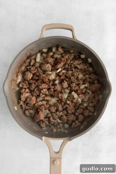 cooking sausage in pan, browning nicely with a wooden spoon.