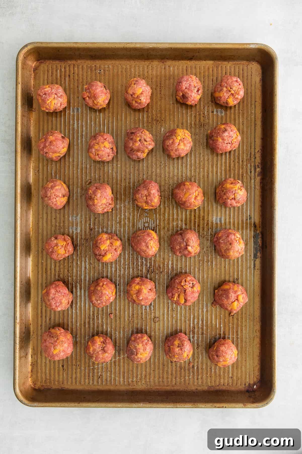 Meatballs Ready for Baking Uncooked cheeseburger meatballs arranged neatly on a greased baking sheet, ready for the oven.