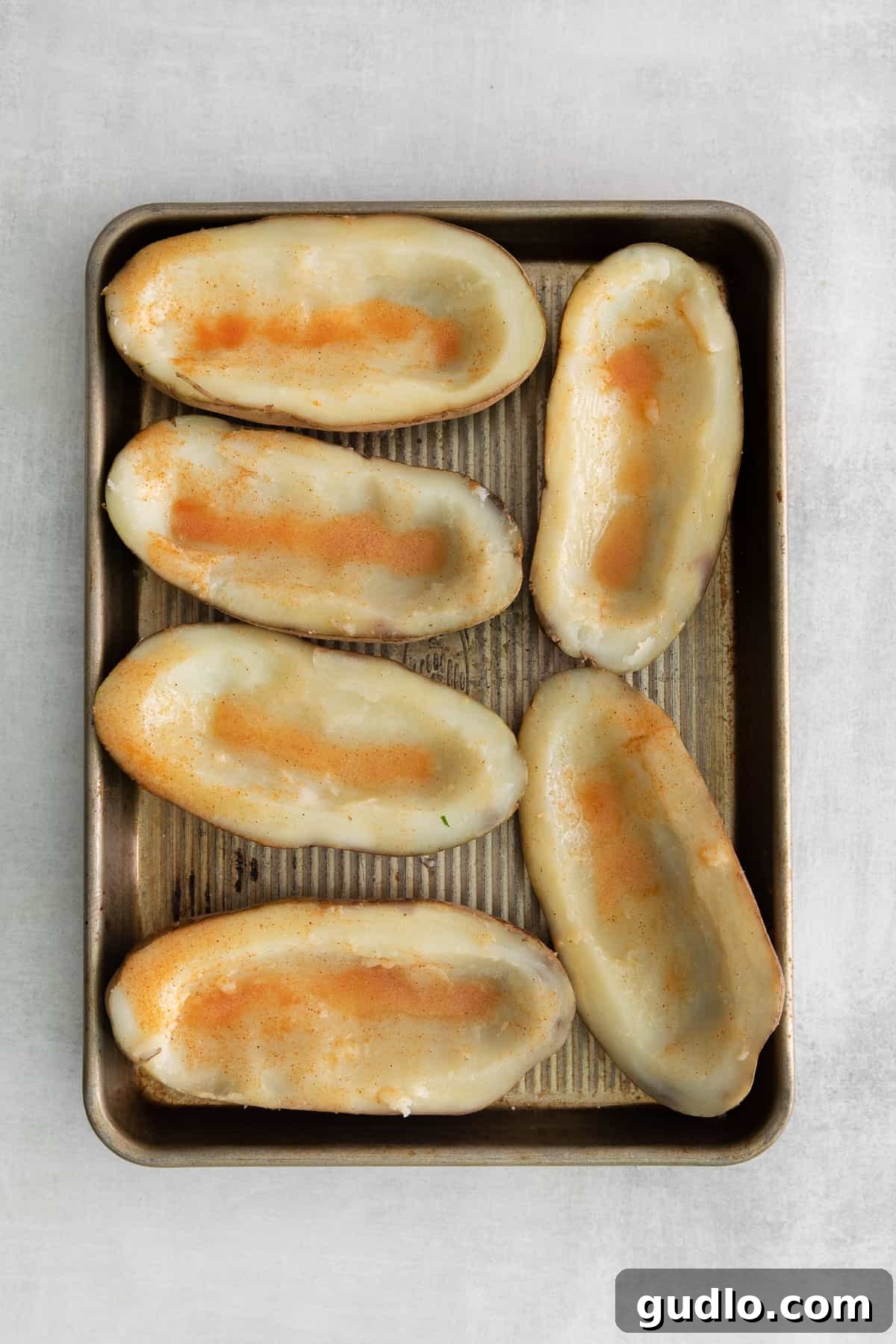 Golden Cheesy Potato Bites 5 Expertly hollowed-out potato skins, brushed with butter and seasoning, arranged on a baking sheet for their first bake.