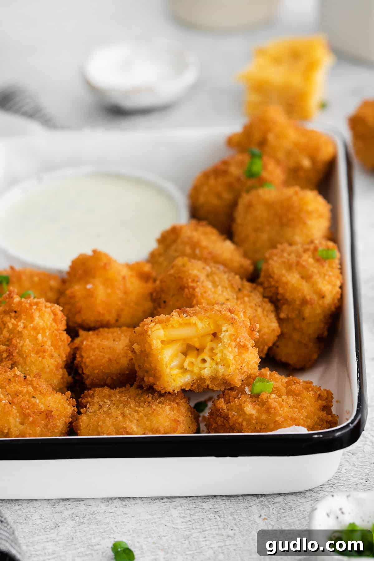Golden-brown fried mac and cheese bites piled generously in a rustic white serving dish, garnished with fresh herbs and ready for enjoyment.