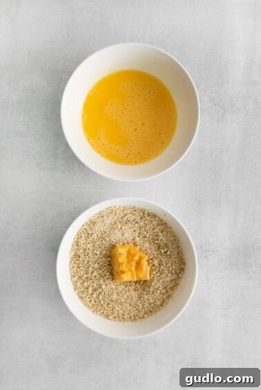 A mac and cheese cube being coated in a bowl of panko breadcrumbs, after being dipped in egg.