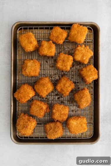 Freshly fried mac and cheese bites resting on a wire rack to drain excess oil, ensuring maximum crispness.